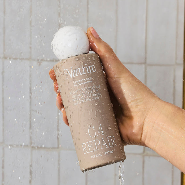 Nutrire c.4 repair conditioner bottle in the shower being held with a hand.