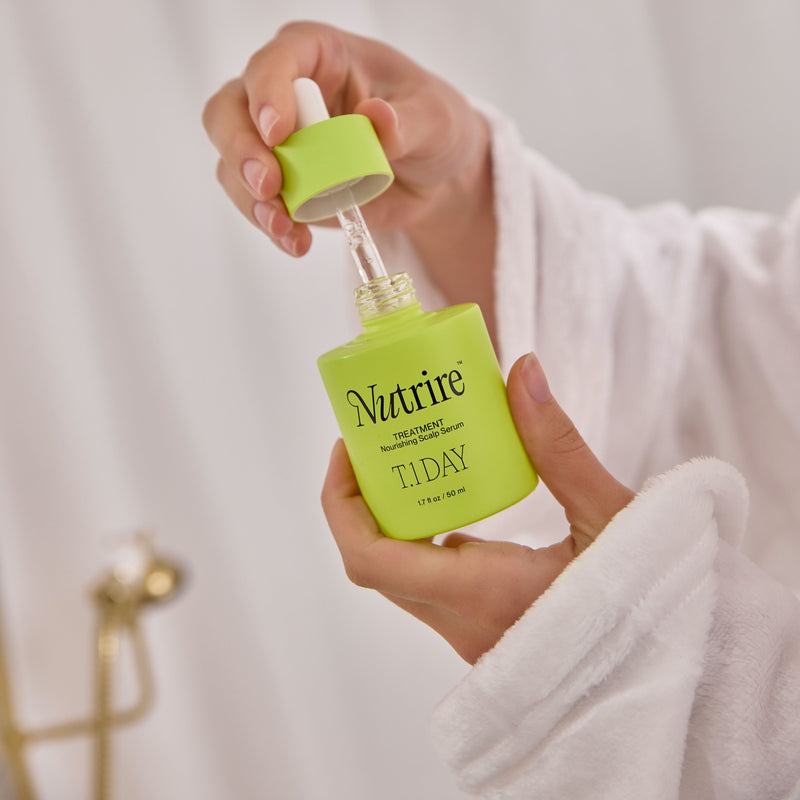 A person in a white robe holds an open lime green dropper bottle labeled Nutrié TIDAY Serum against a soft white background.
